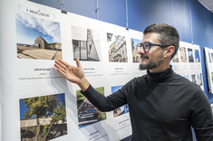 Zbliżenie na mężczyznę w czarnym golfie i w okularach. Mężczyzna wskazuje ręką na zdjęcie.