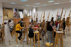 Widok na salę plastyczną. Około 30 uczestników podczas pracy nad swoimi obrazami. Każdy zajmuje miejsce przy sztalugach - drewnianym trójnogu.