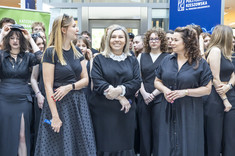 Zbliżenie na trzy kobiety, prowadzące przedmiot. Kobiety ubrane na czarno, stoją obok siebie, uśmiechają się.