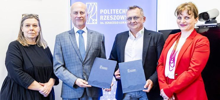 Na zdjęciu stoją obok siebie cztery osoby, dwóch mężczyzn i dwie kobiety po lewej i prawej stronie. Mężczyźni trzymają w ręku dokumenty.  W tle na niebieskiej planszy biały napis Politechnika Rzeszowska.