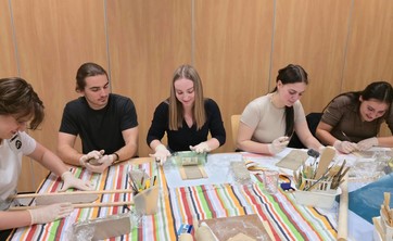 Pięć młodych osób: dwóch mężczyzn i trzy kobiety siedzi przy stole podczas pracy nad przedmiotami z gliny.