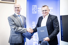Na zdjęciu dwóch mężczyzn w garniturach podaje sobie dłonie, w ręku trzymają dokumenty w okładkach z napisem Politechnika Rzeszowska.  W tle niebieska plansza z białym logiem politechniki - napisem PR w ramce. 