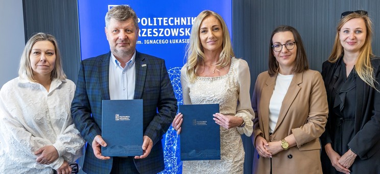 Od lewej prof. A. Sikora, rektor, prof., P. Koszelnik, dr. B. Szafrańska, p. P. Multan, arch. D. Bober. Na zdjęciu na tle ciemnej ściany z wyróżniającym się niebieskim banerem z białym napisem Politechnika Rzeszowska stoi pięć elegancko ubranych osób. Dwie osoby pośrodku trzymają okładki z umowami.