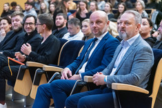 Grupa osób słuchających wykładu. Na pierwszym planie siedzi koło siebie dwóch mężczyzn oficjalnie ubranych.