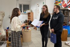 Kobieta i mężczyzna ubrani na czarno, składają podziękowania kobiecie w jasnej bluzce i długiej spódnicy. 