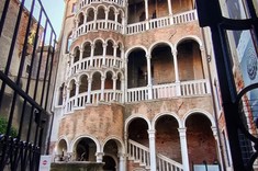 Na zdjęciu widoczna bardzo ozdobna, zabytkowa okrągła klatka schodowa. Schody obudowane są ażurową murowaną ścianą z białymi łukowymi doświetleniami.