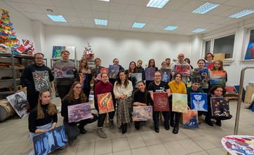 W jasno oświetlonej sali około 30 osób pozujących do wspólnego zdjęcia. Każdy trzyma w rękach barwny obraz.