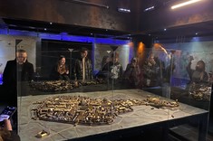 Zdjęcie wnętrza muzeum. Na pierwszym planie duży model historycznej postaci miasta. Jasno brązowa kolorystyka budynków na ciemnoszarym tle podłoża. Model otoczony szklaną ścianką.