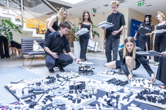 Kilka osób, kobiety i mężczyźni, ubranych na czarno układa na podłodze czarno-białe makiety.