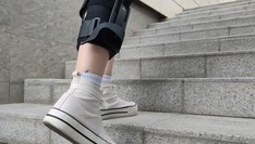 Osoba z ortezą na prawej nodze, wchodząca po schodach.