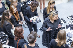 Na zdjęciu grupa studentek i studentów I roku kierunku architektura i koordynator przedmiotu arch. A. Sikora, prof. Uczelni oraz arch. N. Ludwikowska i arch. D. Bober. Zdjęcie wykonane z góry. Wszyscy ubrani na czarno. Studenci trzymają w rękach biało-czarne modele. W tle na podłodze poustawiane również biało-czarne modele.