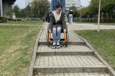 Na zdjęciu dwie studentki – jedna na wózku inwalidzkim, druga w asyście próbują wjechać po schodach przy budynku PRz. 