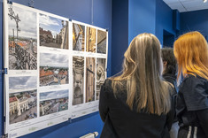 Na ciemnogranatowej ścianie zawieszona jest plansza z kilkoma kolorowymi fotografiami.