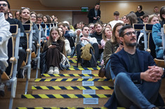 Zbliżenie na słuchaczy wykładu. Część osób siedzi na schodach.