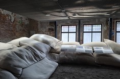 Ciemne, nastrojowe wnętrze. Ceglane ściany, pod sufitem nisko zawieszona stalowa siatka. Pod ścianami wał z białych worków z piaskiem, na podłodze rozsypany piasek.