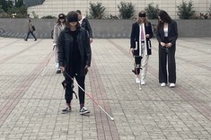 Zdjęcie studentów pod budynkiem PRz. Studenci mają na sobie ortezy, poruszają się z użyciem lasek dla niewidomych i okularów. 