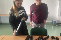 Zdjęcie wewnątrz Sali. Widoczna kobieta wraz z mężczyzną. Przed nimi na stole leżą laski dla niewidomych, rękawice ograniczające czucie, zestaw okularów symulujących wady wzroku. 