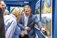 Mężczyzna, autor wystawy, stoi przy jednej z plansz i wskazuje ręką fragment zdjęcia, tłumaczy coś kilku osobom stojącym obok. 