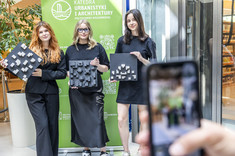 Trzy młode kobiety ubrane na czarno pozują do zdjęcia.  W rękach trzymają biało-czarne makiety.