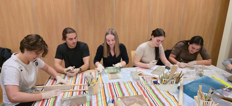 Pięć młodych osób: dwóch mężczyzn i trzy kobiety siedzi przy stole podczas pracy nad przedmiotami z gliny.