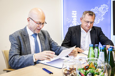 Na zdjęciu dwóch mężczyzn w garniturach podaje sobie dłonie, w ręku trzymają dokumenty w okładkach z napisem Politechnika Rzeszowska.  W tle niebieska plansza z białym logiem politechniki - napisem PR w ramce. 