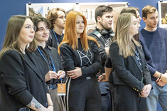 Grupa kilkunastu młodych osób, przeważnie ubranych na czarno, kieruje wzrok przed siebie.