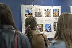 Uczestnicy wystawy przyglądaj się planszy ze zdjęciami. Zdjęcie zrobione od tyłu.