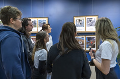 Grupa kilku osób przygląda się wiszącym fotografiom na ścianie,