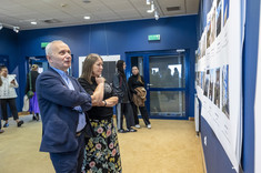 Mężczyzna w ciemnym garniturze i kobieta przyglądają się wystawie.  W tle inni uczestnicy wystawy.