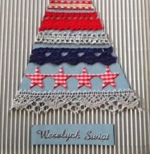 Kartka świąteczna. Na srebrnym tle wycięty prosty, trójkątny niebieski kształt choinki. Na trójkącie umieszczone równoległe poziome pasy z szarej, granatowej i czerwonej koronki. Na czubku choinki szara gwiazda.